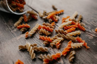 çok renkli çiğ spiral makarna, turuncu ve sarı, koyu ahşap bir zemindeki cam kavanozdan serpilmiş.