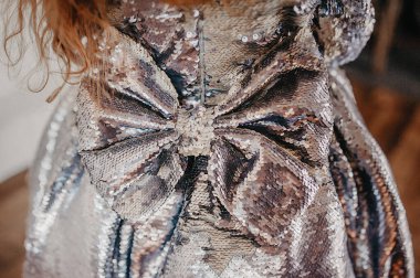 Pullardan yapılmış, arkasında kocaman bir fiyonk olan parlak gümüş pullu bir kız için çok güzel bir elbise.