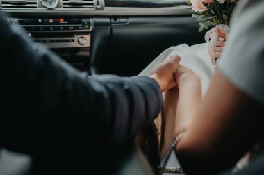 Gelin ve damat, düğünün arka planında siyah deriden arabanın içindeki ele sıkıca tutunan yüzü göremez.