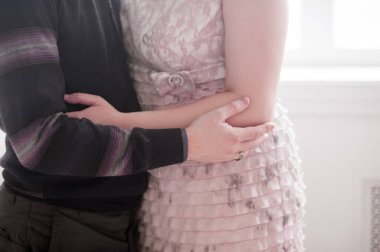 Yüzleri olmayan hafif yatak renklerinde bir fotoğraf. Aşıklar el ele tutuşur ve birbirlerine çok yakın dururlar.