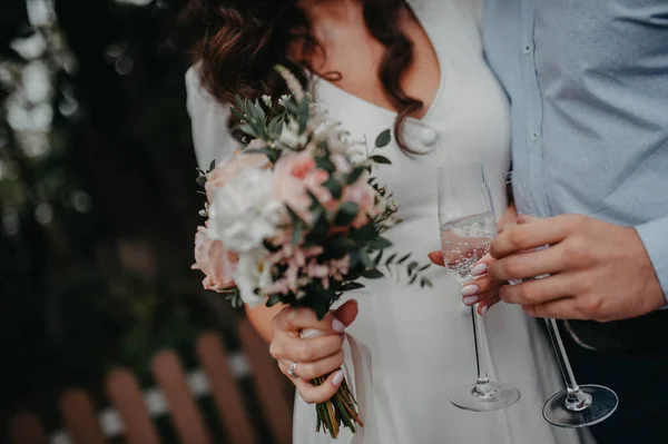 the groom in a blue shirt and the bride in a simple elegant white dress drink sparkling non-alcoholic water in wedding glasses