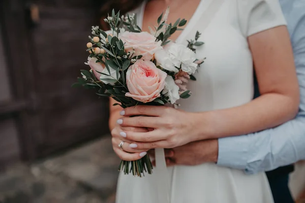 男のハード後ろから白いドレスの女性を抱擁し 一緒に彼らはピンク牡丹と白いバラから花嫁のシックなエレガントな花束を保持します — ストック写真