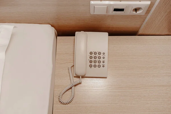 not a modern white wired telephone with buttons on a beige wooden bedside table