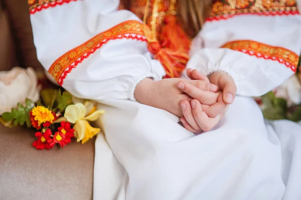 children\'s hands are folded together for prayer and reflection on a person in a traditional folk dress of white color with red embroidery from threads