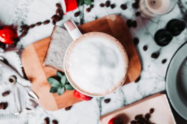 Zarif kahve manzarayı tepeden bozuyor. Bir fincan dolusu süt köpüğü mermer bir sehpanın üzerinde Türk kahve fincanı, dağınık kahve çekirdekleri, kahve kapsülleri, çilekler ve mumlar..