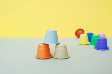 Gri-sarı bir zemin üzerinde gri, bej ve turuncu kapsüller bir piramit şeklinde üst üste ve diğer çok renkli kapsüllerin arka planında