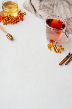 Böğürtlenli vitamin çayı, bal, Rowan ve deniz dikenli böğürtlen, tarçın çubukları ve örülmüş bej bir kazakla arka planda kuru karanfil. dikey olarak, metin için boşluk