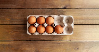 Uzun format pankart, karton bir kutuda kahverengi yumurtalar kahverengi ahşap bir masa üzerinde boş hücreler, üst görünüm