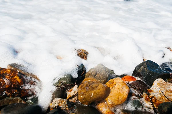 泡とスプレーロールで澄んだ海の水の波とラウンド滑らかなオレンジの石に休憩 — ストック写真