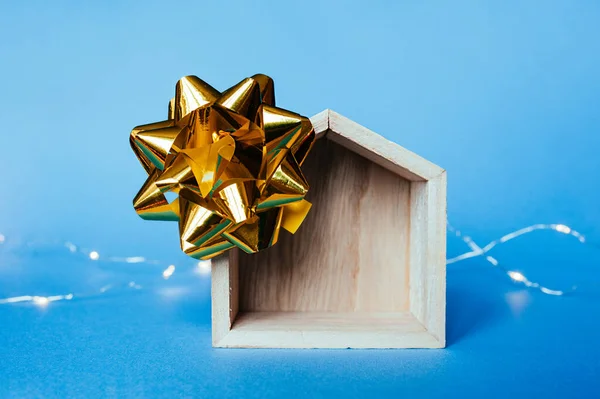 gold foil decor bow on a wooden toy empty house and garlands on a blue background at the back.