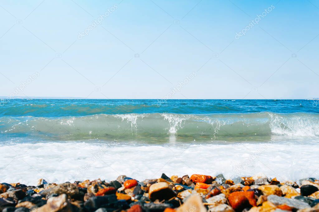 Strong waves in a clear emerald sea with a rocky bottom. Smooth orange stones on the seashore. Sea raging element.