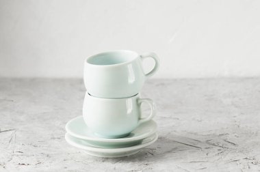 Doğu tarzında iki boş porselen, açık mavi bardak ve iki çay tabağı açık beton arka planda yan yana duruyorlar.