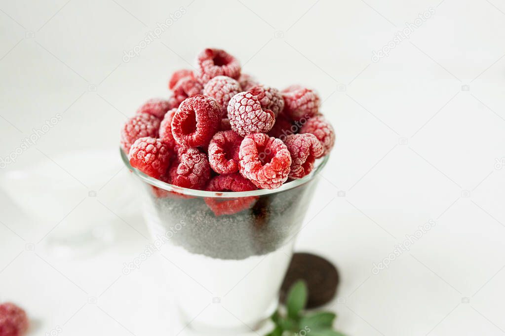 Fresh frozen red beautiful raspberries in a tall glass on a light table. Summer menu, recipes with seasonal ripe berries