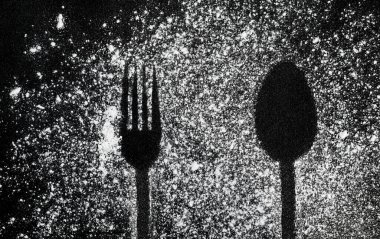 Çatal ve kaşıktan siyah bir arkaplanda izler var. Koyu bir zemine dağılmış beyaz toz ve bulaşık izleri. Çatal bıçak takımının alışılmadık bir görüntüsü.