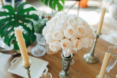 Eski usul servis edilen ahşap bir masada duran taze, temiz, aynı güllerden oluşan beyaz bir buket. Klasik tarzda düğün dekoru..