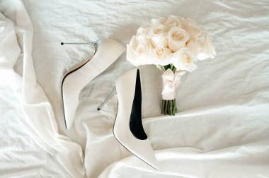 Uzun şeffaf topuklu sivri uçlu şık beyaz düğün ayakkabıları ve buruşuk pamuklu bir kumaşta düğün buketi. Yukarıdan manzara. Gelin için aksesuarlar.