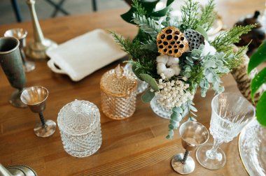 Eski bir metal çatal bıçakla eski usul ahşap bir masaya servis yapmak. Bir buket kuru çiçek ve kuru nilüfer çiçeği..