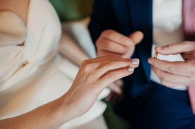 Mavi takım elbiseli damat, gelinin eline beyaz şık bir elbise giymiş altın bir yüzük takıyor. Yeni evlilerin elleri, yüzleri yok..