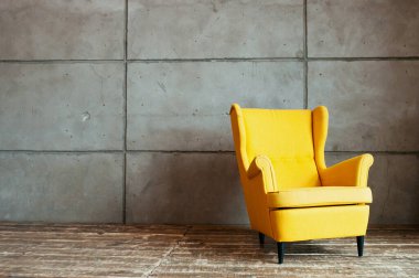Gri, düz olmayan beton bir duvara ve koyu ahşap bir zemine karşı serin, güçlü sarı bir koltuk. Çatı katı biçiminde minimalist iç mimari.
