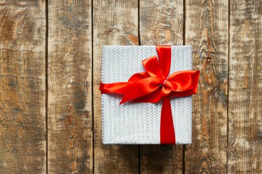 Kırmızı saten kurdeleli büyük beyaz bir hediye kutusu ve siyah ahşap arka planda büyük bir fiyonk..