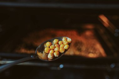 Nohut taneleri, arkaplandaki metal kaşıkta, hazır olan nohut taneleri, siyah bir fırında pişirilir. Evde sağlıklı yemek pişirmek..