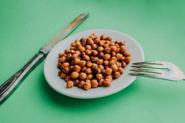 Baharatlı kızarmış bezelyeli beyaz farvor tabağı, temiz yeşil arka planda eski gümüş kaşık ve çatal. Sağlıklı yiyeceklerin kolay pişirilmesi.