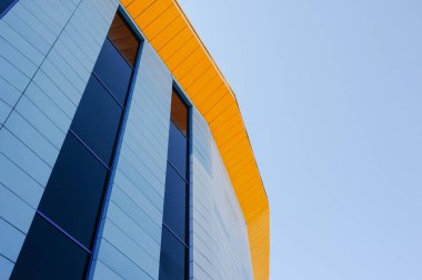 Parlak mavi gökyüzünün arka planında sarı çatılı şık geometrik mavi cam bina.