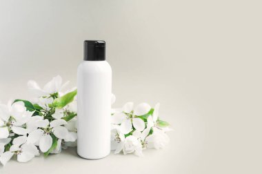 Beyaz arka planda yeşil yapraklı, yemyeşil çiçek filizleri açan siyah şapkalı beyaz bir şişe. Kozmetik çizimi. Cilt ve vücut bakımı eşleşir