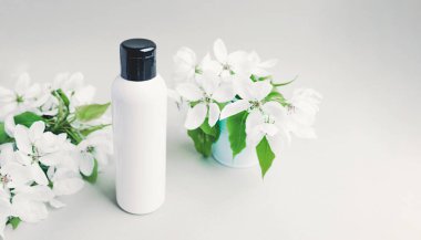 Afiş beyazı, beyaz, siyah kapaklı, beyaz arka planda yeşil yapraklı, yemyeşil çiçek filizleri olan temiz bir şişe. Kozmetik çizimi. Cilt ve vücut bakımı eşleşir