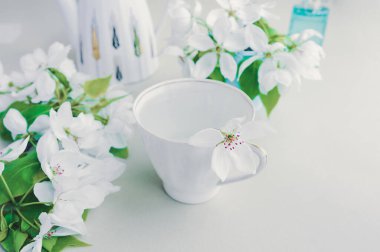 Su ve beyaz narin çiçekli beyaz porselen bardak, beyaz çaydanlık ve armut çiçekli mavi vazo. Kendine zaman ayır, meditasyon, akıl sağlığını destekleme.