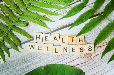 inscription health wellness is made of small wooden blocks printed on a wooden background with a green fresh leaf of greenery. new normal ready-made modern content clipart