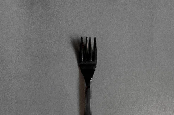 simple clean black plastic fork on a flat clean gray background with a hard shadow. The minimalist monochrome photo of dishes.