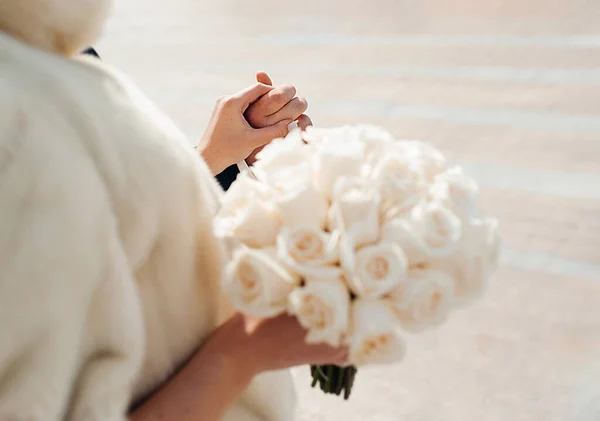 結婚式で恋人の手がしっかりと開催されます 前景の少女の手の中に新鮮な同じバラの白いブライダル花束 — ストック写真