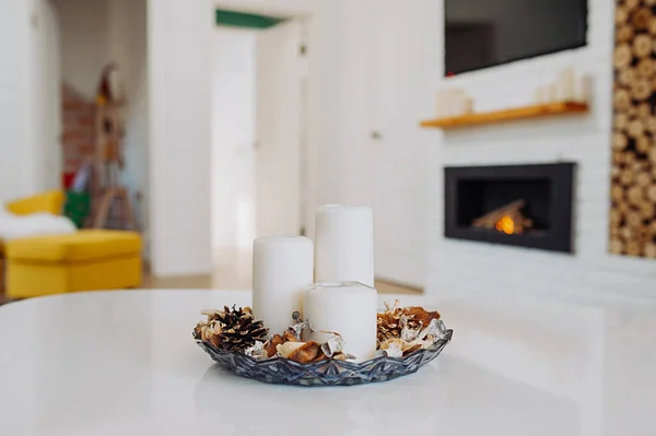 white candles in a sconce for aromatherapy on the background of a cozy apartment in a white Scandinavian style with a fireplace and stacked wood