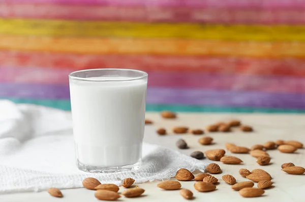 transparent mug full of milk on the background of beautifully spread almonds. Almond milk against a bright multicolored wall