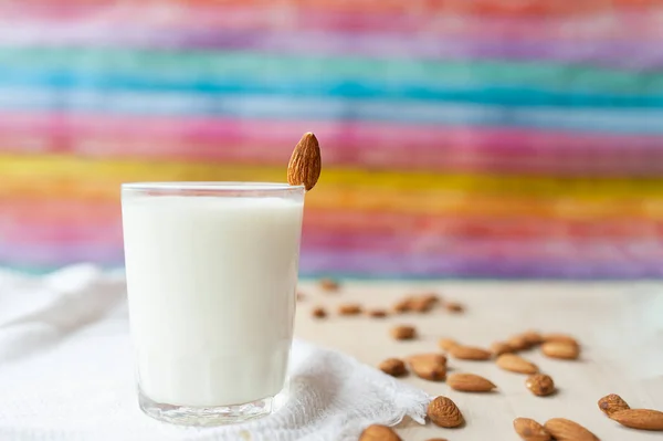 transparent mug full of milk on the background of beautifully spread almonds. Almond milk against a bright multicolored wall. milkshake with nuts