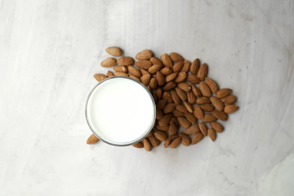 transparent mug full of milk on the background of beautifully spread almonds. Almond milk, top view