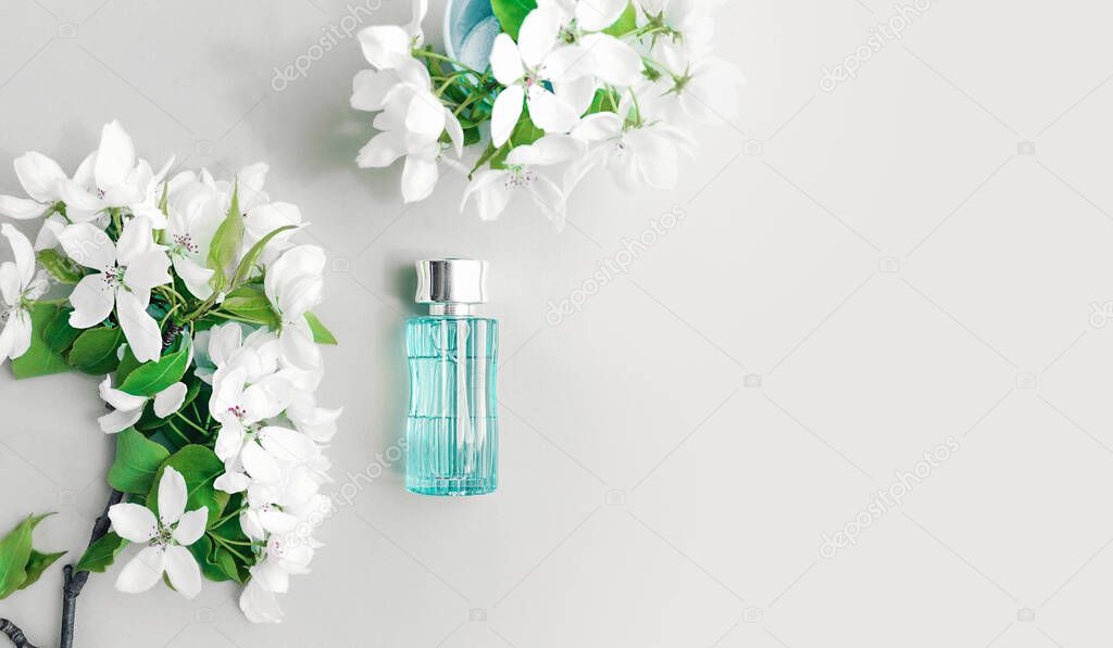 Blue transparent glass bottle with a silver cap and branches of white lush fresh flowers. Cosmetic and aromatic layout for advertising and content. Top view, place for text.