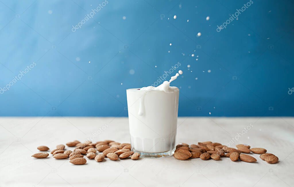 splash and drops from a clear mug full of milk with beautifully arranged almonds. Almond milk on a blue background