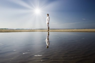 Tıbbi maskeli bir adam sahilde yürüyor.