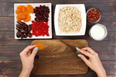 Kız ona kahvaltı hazırlıyor. Kesme Kuruyemiş haline yulaf lapası bir kesme tahtası üzerinde. Yararlı ve sağlıklı bir kahvaltı. koyu ahşap arka plan, üstten görünüm.