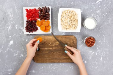 Kız ona kahvaltı hazırlıyor. Kesme Kuruyemiş haline yulaf lapası bir kesme tahtası üzerinde. Gri bir arka planda en iyi görünüm yararlı ve sağlıklı bir kahvaltı.