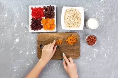 Kız ona kahvaltı hazırlıyor. Kesme Kuruyemiş haline yulaf lapası bir kesme tahtası üzerinde. Gri bir arka planda en iyi görünüm yararlı ve sağlıklı bir kahvaltı.