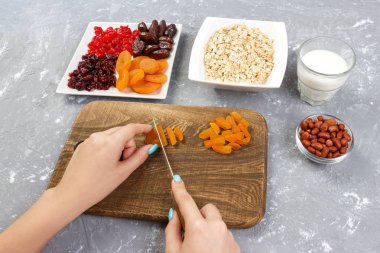 Kız ona kahvaltı hazırlıyor. Kesme Kuruyemiş haline yulaf lapası bir kesme tahtası üzerinde. Gri bir arka planda en iyi görünüm yararlı ve sağlıklı bir kahvaltı.