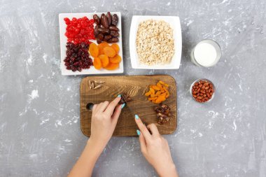 Kız ona kahvaltı hazırlıyor. Kız onun tarihi meyve yulaf lapası kesme tahtası olarak keser. Gri bir arka planda en iyi görünüm yararlı ve sağlıklı bir kahvaltı.