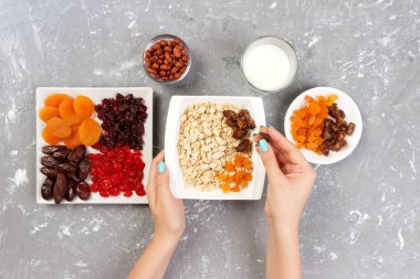 Yararlı ve sağlıklı bir kahvaltı. Kız onu müsli kahvaltı için hazırlanıyor. Kız kendini Kuru meyve yulaf lapası üstten görünüm, gri bir arka plan koyar.