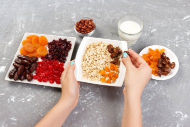 Kız onu müsli kahvaltı için hazırlanıyor. Kız kendini yulaf lapası kurutulmuş meyve koyar. Gri bir arka planda en iyi görünüm yararlı ve sağlıklı bir kahvaltı.