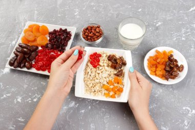 Yararlı ve sağlıklı bir kahvaltı. Kız onu müsli kahvaltı için hazırlanıyor. Kız kendini Kuru meyve yulaf lapası üstten görünüm, gri bir arka plan koyar.