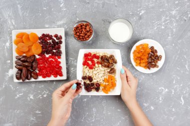 Kız onu müsli kahvaltı için hazırlanıyor. Kız kendini yulaf lapası kurutulmuş meyve koyar. Gri bir arka planda en iyi görünüm yararlı ve sağlıklı bir kahvaltı.
