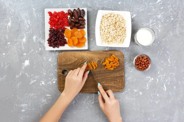 Kız ona kahvaltı hazırlıyor. Kesme Kuruyemiş haline yulaf lapası bir kesme tahtası üzerinde. Gri bir arka planda en iyi görünüm yararlı ve sağlıklı bir kahvaltı.